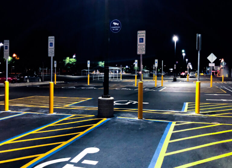 Yellow bollards, ADA parking signs, and pavement markings in a parking lot at night.
