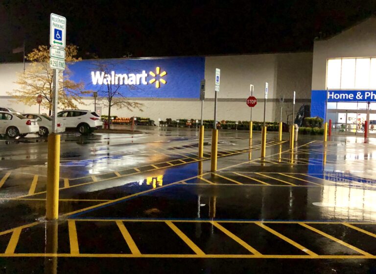 Yellow bollards, ADA signs, and pavement markings near a Walmart entrance at night.