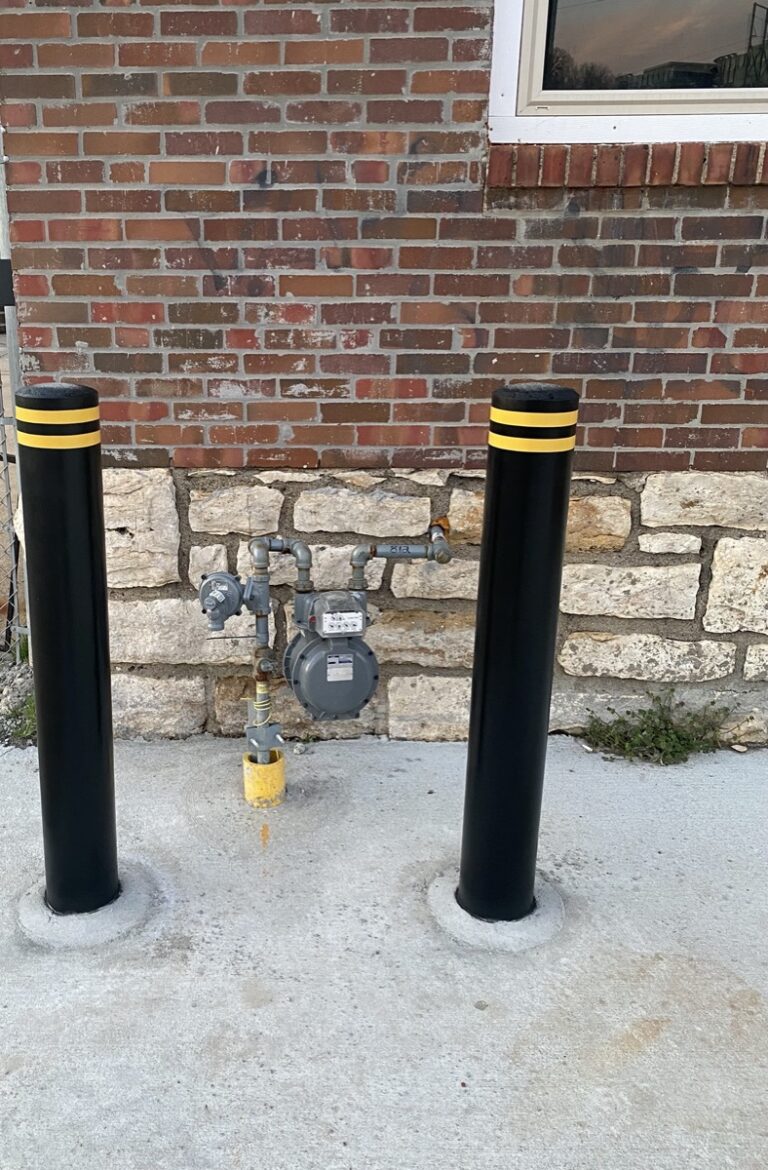 Black bollards protecting a gas meter beside a brick building in Kansas City, Missouri.