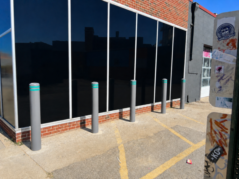 Gray protective bollards installed outside a storefront with large windows.