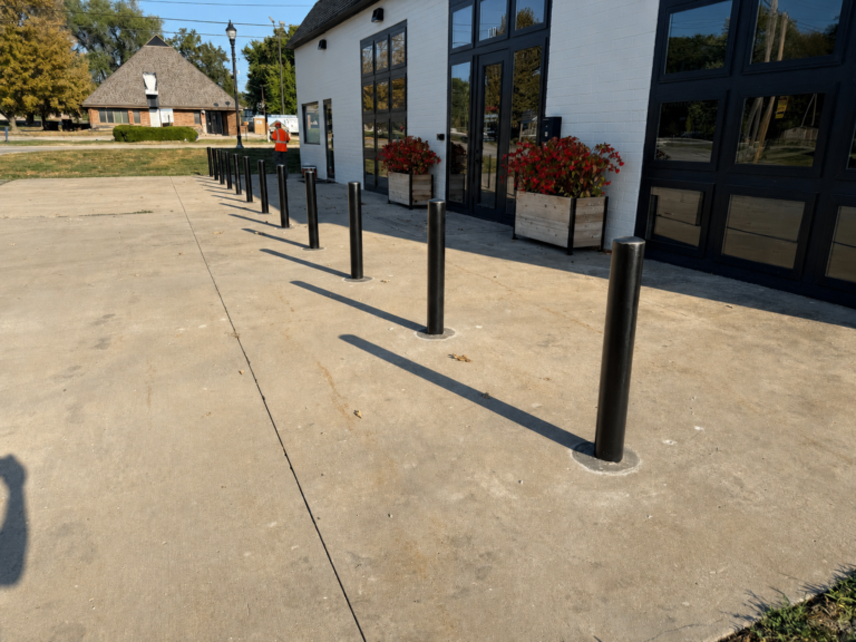 Black storefront security bollards installed along a sidewalk outside a commercial building.