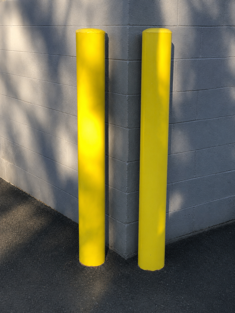 Two yellow bollards installed beside a building corner.